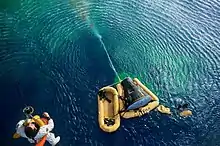 Photograph of the Gemini 10 spacecraft in the ocean and Young being hoisted from it