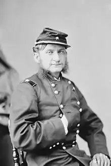 Black and white photo shows a youthful-looking man with his right hand thrust into his jacket Napoleon-style. He wears a kepi and a dark military uniform with the one star of a brigadier general on his shoulder tabs.