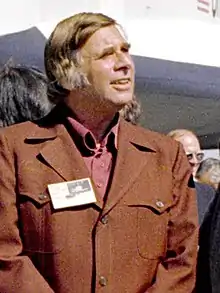 A man wearing a brown suit looks up to the right.