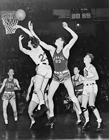 Two basketball players are going after a basketball, while four other players are watching from behind.