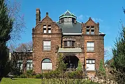 Asymmetrical, two-and-a-half-story stone house with an ornate dormer at the roof peak