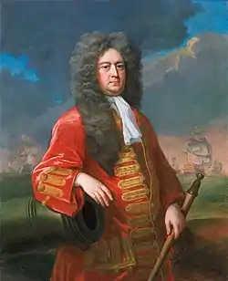 Painting of Sir George Rooke in a long flowing wig and a red coat with gold frogging, resting his right arm on a cannon and holding a rammer in his left hand. A fleet of ships is visible in the background.