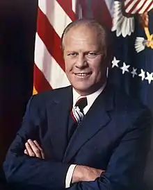 man in business suit, American flag and Presidential flags in background