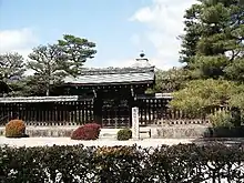 Structure with pointy roof behind a wooden fence and gate.