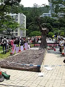 large bronze statue and relief laid out on paved walkway cordoned off with blue and white tape but surrounded by curious visitors