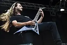 Close-up of Christian Andreu, long hair flying, playing a guitar with a cutaway bottom