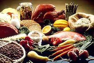 Table set with red meat, bread, pasta, vegetables, fruit, fish, and beans