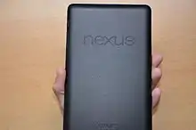 View of the back of a rectangular device held in a hand. The dimpled surface features two prominent words, "Nexus", and "Asus".