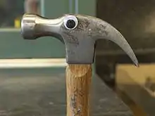 One googly eye attached to the side of the metal piece of a hammer