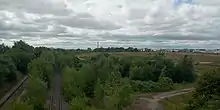 A patch of waste ground with railway lines on the left and industrial buildings in the distance