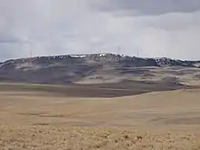 Turbines of the Gordon Butte Wind Farm sit atop the plateau, as seen from the east, with brown rolling prairie in the foreground.