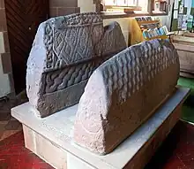 Image 27So-called "Saint's tomb" (left), and "Warrior's tomb" (right), two hogbacks in St. Mary's church, Gosforth. Typically high and narrow Cumbrian style, in the shape of a building with a roof, eaves and walls. The Saint's tomb has a crucifixion on the end, the Warrior's tomb has a procession of armed men (from History of Cumbria)