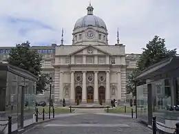 Building with central cupola and Ionic columns, with modern gatehouses in foreground