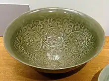 A green bowl with a pattern of circular flowers with small, thin petals set over a background of vines glazed into it.