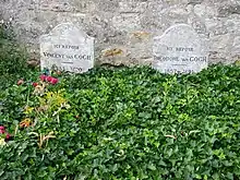 Two graves and two gravestones side by side; heading behind a bed of green leaves, bearing the remains of Vincent and Theo van Gogh, where they lie in the cemetery of Auvers-sur-Oise. The stone to the left bears the inscription: Ici Repose Vincent van Gogh (1853–1890) and the stone to the right reads: Ici Repose Theodore van Gogh (1857–1891)