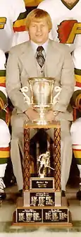 Gregg Pilling sitting behind the Lockhart Cup in a team photo of the 1976-77 Philadelphia Firebirds.