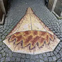 On Peter Street in Dundee, there is a mosaic on the ground commemorating Grisell Jaffray, the last woman to be burnt as a witch there. There are two elements to the mosaic, one representing fire and the other representing water. This image is of gold and red mosaic tiles representing fire, surrounded by cobble stones.