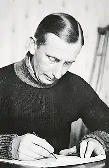 Black and white photo of Grove seated at a desk, looking down and writing.