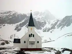 A white wooden church nestled within snow-covered mountains.