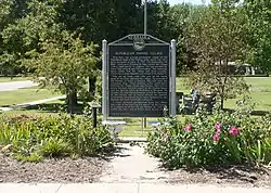 Sign in park, with flowers and trees and bench