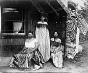 Tourist guides Sophia Hinerangi (standing), Kati and another, outside Hinemihi meeting house at Te Wairoa. Taken by Elizabeth Pulman about 1881