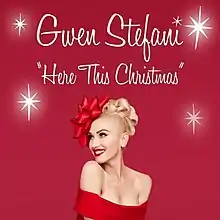 A red background displays a color photograph of American singer Gwen Stefani, dressed in a sleeveless red gown and adorned with a red ribbon on her head, worn as a headband; the image also contains 4 large white sparkles and the words: Gwen Stefani, "Here This Christmas"