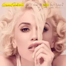 Stefani's face is shown while she pulls a lock of hair down in front of her face with her finger.