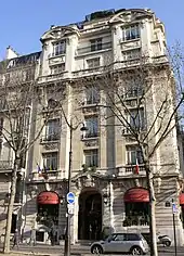 A six-storey building at the corner of a terrace lined in front by bare trees