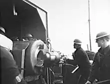 Gunners wearing steel helmets load a shell into a large calibre weapon