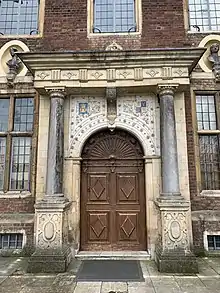 A photograph of the wooden front door of the house, surrounded by early 17C architectural embellishments such as columns and carvings