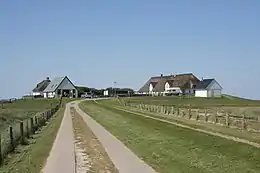 Three houses, two of them with thatched roofs, and a shed are located on a hill at the end of a field track