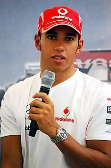 Lewis Hamilton wearing silver T-shirt and speaking into a microphone