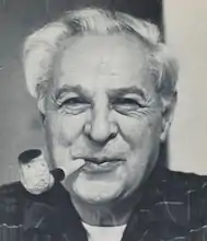 black and white headshot image of an older white man with white hair smoking a pipe