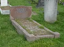 A red granite gravestone in a grassy cemetery