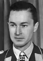 Black-and-white photograph showing the face and shoulders of a young man in uniform. The front of his shirt collar bears an Iron Cross decorations, black with light outline.