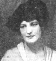 A white woman wearing a dark hat and a light colored dress or blouse