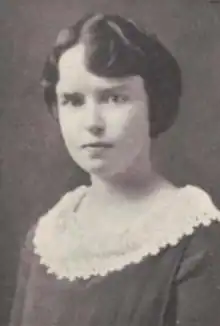 A young white woman with dark hair, wearing a dark dress with a wide, round lace collar detail