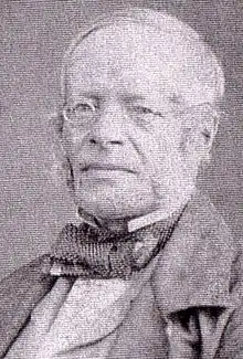 Photo of the head and shoulders of a man of about 70, wearing a bow tie and mutton-chop whiskers with a clean-shaven throat and chin