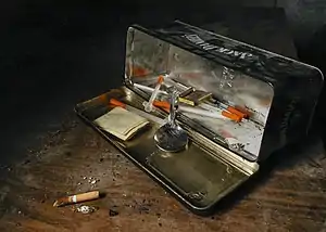 A black metal box turned on its side and opened to show instruments used for heroin use, including a silver spoon and syringes