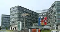 A light gray building of steel and glass with the flags of Hamburg, Germany, and Europe.