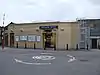 A beige-bricked building with a rectangular, blue sign reading "HIGH BARNET STATION" in white letters all under a blue sky with white clouds