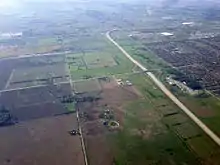 An aerial photograph of Highway 407 travelling north through farmland towards an interchange with Highway 401. Subdivisions of Mississauga are visible to the right.