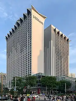 Ground-level view of two concrete towers; the one on the left is more prominent, and has a windowless anterior facade with triangular structures protruding from the roof.