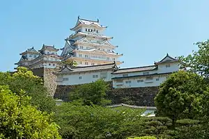 A white castle with a large five-storied main tower and two smaller towers all built on a stone base.