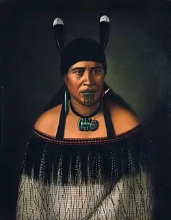 Image 48Hinepare of Ngāti Kahungunu, is wearing a traditional korowai cloak adorned with a black fringe border. The two huia feathers in her hair, indicate a chiefly lineage. She also wears a pounamu hei-tiki and earring, as well as a shark tooth (mako) earring. The moko-kauae (chin-tattoo) is often based on one's role in the iwi. (from Culture of New Zealand)