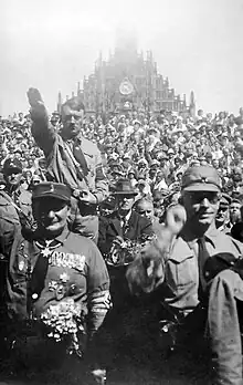 A monochrome image of a mass of people outside of a church facing the viewer performing Nazi salutes.