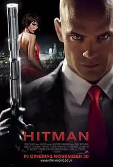 In the distance is a woman in a red dress. In the foreground is a bald man wearing a suit and red tie, holding a gun, pointed upwards