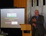 Minister Pete Hodgson leaning on a lectern, with an image displayed on a screen