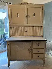 A free-standing light-brown piece of furniture with a workspace and drawers with storage