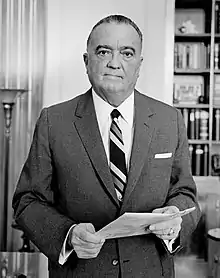 A portrait of a man, standing, holding papers